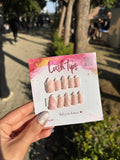 Card with false nail tips labeled 'Lush Tips' held by a person outdoors.