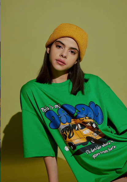 Person wearing a green oversized t-shirt with a graphic design on a solid background